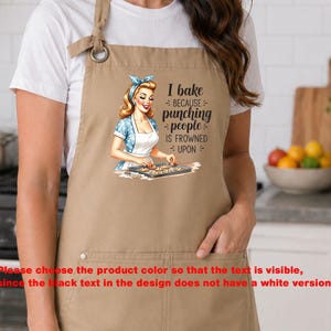 Könnte beinhalten: Beige Schürze mit einer Retro-Illustration einer backenden Frau. Auf der Schürze steht der Text "I bake because punching people is frowned upon". Sie hat eine Vordertasche und einen verstellbaren Nackenriemen.