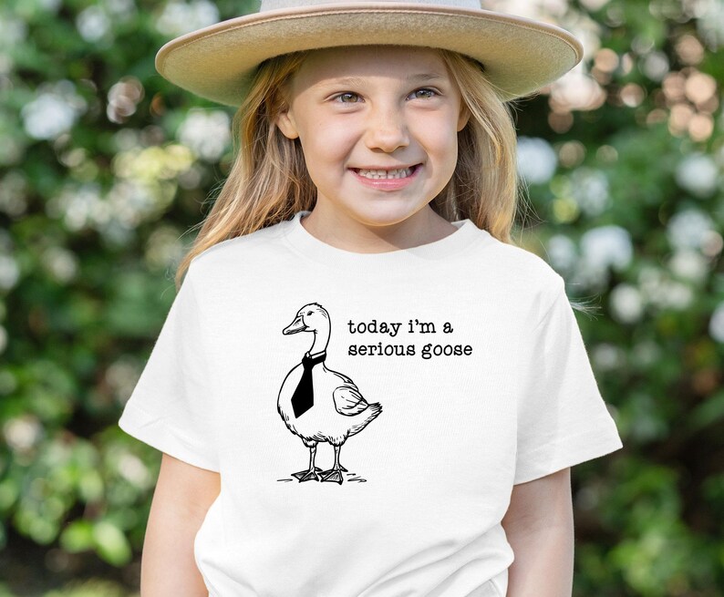 Pu&ograve; includere: Una maglietta bianca con un'illustrazione in bianco e nero di un'oca con una cravatta. Il testo "today i'm a serious goose" &egrave; stampato sulla maglietta.