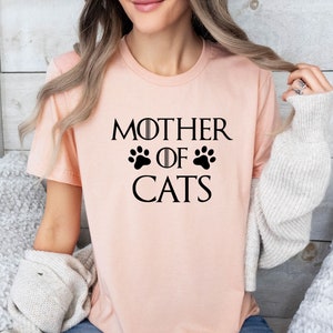 May include: A pink t-shirt with the text "Mother of Cats" in black, featuring a paw print design.