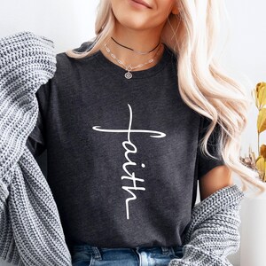 Peut inclure: Un t-shirt gris fonc&eacute; avec une croix blanche et le mot "foi" &eacute;crit verticalement au centre de la croix.