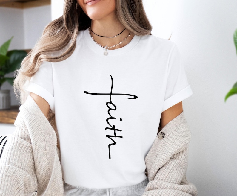 Peut inclure: T-shirt blanc avec une croix noire et le mot "foi" &eacute;crit verticalement au centre de la croix.