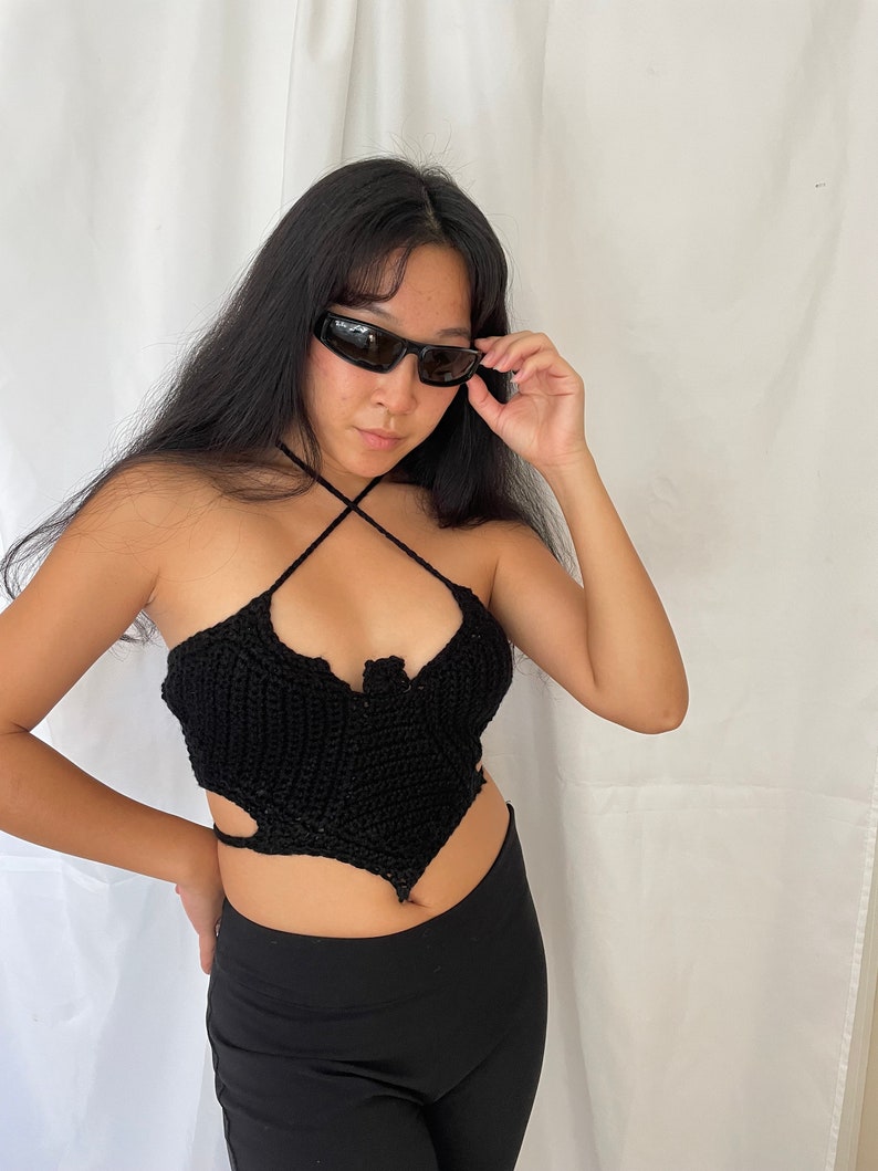 Pode incluir: Um top halter preto de croch&ecirc; com um design de al&ccedil;a cruzada. O top tem um decote em forma de cora&ccedil;&atilde;o e recortes nas laterais.