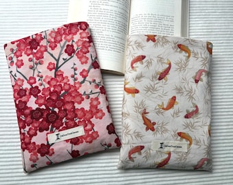 May include: Two fabric book covers. One has a pink background with red cherry blossoms. The other has a white background with orange and pink koi carp and bamboo. Both have a small label with text.