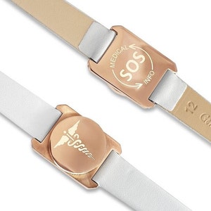 Könnte beinhalten: Ein weißes Lederarmband mit einem roségoldenen medizinischen Warnhänger. Der Anhänger hat auf der einen Seite ein medizinisches Symbol und auf der anderen Seite die Worte "MEDICAL SOS INFO".