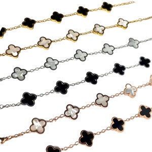 Op de afbeelding: Vier zilveren kettingarmbanden met klavertjevier-charms. Twee armbanden hebben zwarte emaille klavertjes, en twee hebben witte parelmoer klavertjes.