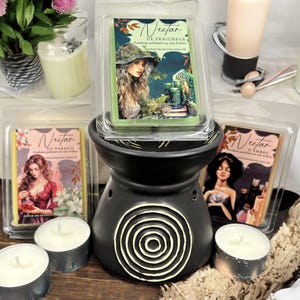 Peut inclure: Trois galets de cire parfumée avec des illustrations de femmes et le texte "Nectar de Fraicheur", "Nectar de Paradis" et "Nectar d'Ambre" sur un chauffe-cire en céramique noire avec un motif circulaire.