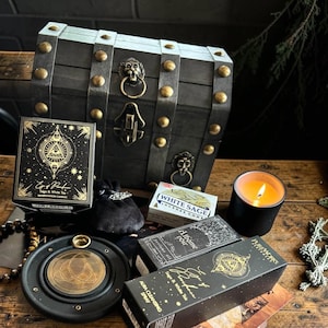 Può includere: Un forziere in legno scuro con borchie in ottone e anelli a testa di leone, accompagnato da candele di manifestazione Eye of Ra, coni di incenso White Sage, una candela nera in vetro, un sacchetto nero e un bruciatore di incenso con triquetra.