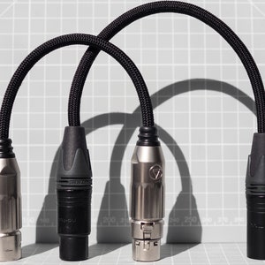 Peut inclure: Deux câbles tressés noirs avec des connecteurs métalliques. Un connecteur est argenté avec une poignée en caoutchouc noir et l'autre est noir avec une poignée en caoutchouc noir.