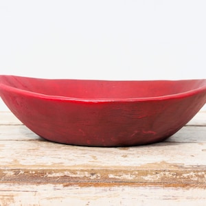 Puede incluir: Un cuenco de madera rojo con un acabado rústico. El cuenco tiene forma ovalada y un borde ligeramente elevado.