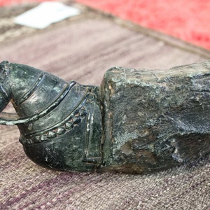 Puede incluir: Una escultura de piedra verde oscuro de una cabeza de caballo con un arnés, montada sobre una base de piedra rugosa y texturizada.
