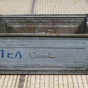 Può includere: Una cassetta di metallo grigia con la scritta "TEA" e il logo "Fumi" stampato sul davanti.