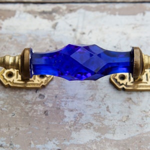 Könnte beinhalten: Ein blauer gläserner Türgriff mit goldenen Metallakzenten. Der Griff ist facettiert und hat eine diamantartige Form.