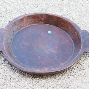 Puede incluir: Una bandeja redonda de madera grande con dos asas. La bandeja es de color marrón oscuro y tiene un aspecto desgastado y rústico.