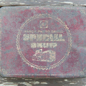 Può includere: Una scatola di latta vintage di colore rosso con un design circolare dorato. Il testo "PANCH PHOTO BRAND SPECIAL" è stampato in lettere dorate sulla scatola.