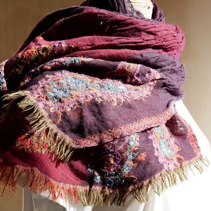 May include: A burgundy and purple shawl with intricate embroidered floral patterns and gold fringe.