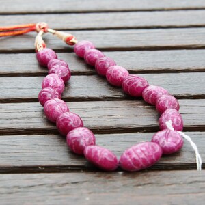 May include: A pink gemstone necklace with oval-shaped beads. The necklace is made of natural stones and is strung on a thin cord.