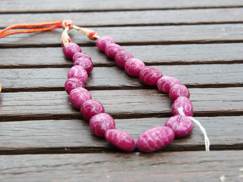May include: A pink gemstone necklace with oval-shaped beads. The necklace is made of natural stones and is strung on a thin cord.