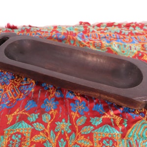 Può includere: Un vassoio da portata in legno marrone scuro con due manici. Il vassoio è intagliato nel legno e ha una finitura liscia e lucida.