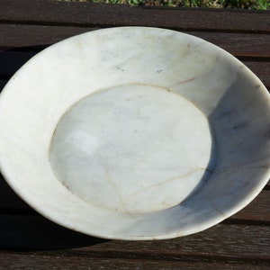 Puede incluir: Un plato de servir redondo de mármol blanco con un borde ligeramente elevado. El plato es liso y pulido.