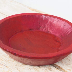 Puede incluir: Un cuenco de madera de color rojo oscuro con un interior liso y redondeado. El cuenco está hecho de madera natural y tiene un aspecto rústico y artesanal.