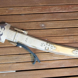 May include: A silver and ivory-coloured dagger with intricate carvings and a wooden handle. The dagger is lying on a wooden surface.