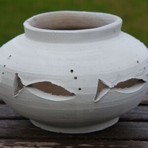 Può includere: Vaso in ceramica bianca con disegni di pesci ritagliati. Il vaso ha una forma arrotondata e un'ampia apertura.