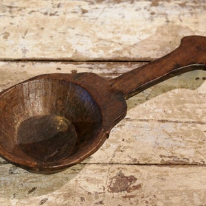 Puede incluir: Un cucharón de madera marrón oscuro con un cuenco redondeado y un mango largo. El mango tiene una forma única con un extremo redondeado.