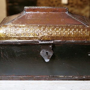 May include: A small, rectangular wooden box with a hinged lid. The box is decorated with a gold-coloured metal trim and has a metal latch. The box is black with a dark brown lid.