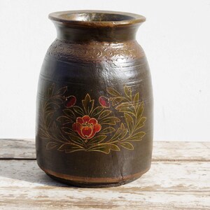 May include: A dark brown wooden vase with a floral design painted in gold, red, and green. The vase has a rounded body and a slightly flared opening.