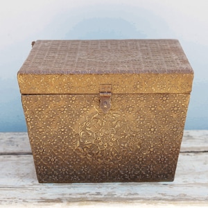 Puede incluir: Una pequeña caja de madera adornada con una tapa con bisagras y un cierre de latón. La caja está decorada con un patrón floral y tiene un acabado dorado.