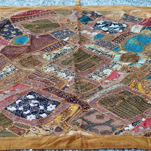 Puede incluir: Una colcha de retazos colorida con un borde de gamuza marrón. La colcha está hecha de varias telas y texturas, incluyendo terciopelo, satén y bordado. La colcha está decorada con cuentas, lentejuelas y otros adornos.