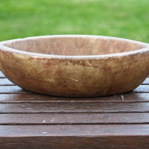 Könnte beinhalten: Eine rustikale Holzschale in hellbrauner Farbe und leicht ovaler Form. Die Schale hat ein abgenutztes, gealtertes Aussehen mit dezenten roten und braunen Streifen.