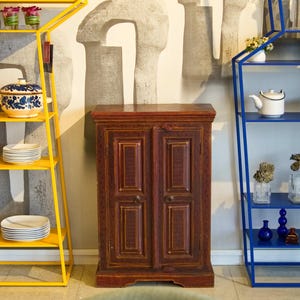 Könnte beinhalten: Ein Raum mit dekorativen Regalen und einem Holzschrank. Ein gelbes Metallregal zeigt blau-weiße Keramik und Teller. Ein blaues Metallregal beherbergt eine Teekanne, Tassen und Vasen. Ein dunkler Holzschrank steht zwischen den Regalen.