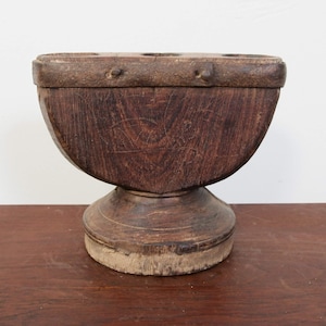 Könnte beinhalten: Ein dunkelbrauner Kerzenhalter aus Holz mit abgerundeter Basis und rechteckiger Oberseite mit fünf Löchern für Kerzen. Der Halter hat ein rustikales, antikes Aussehen.