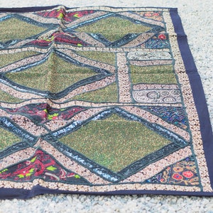 May include: A green and black patchwork throw rug with diamond patterns and intricate embroidery. The rug has a dark blue border.