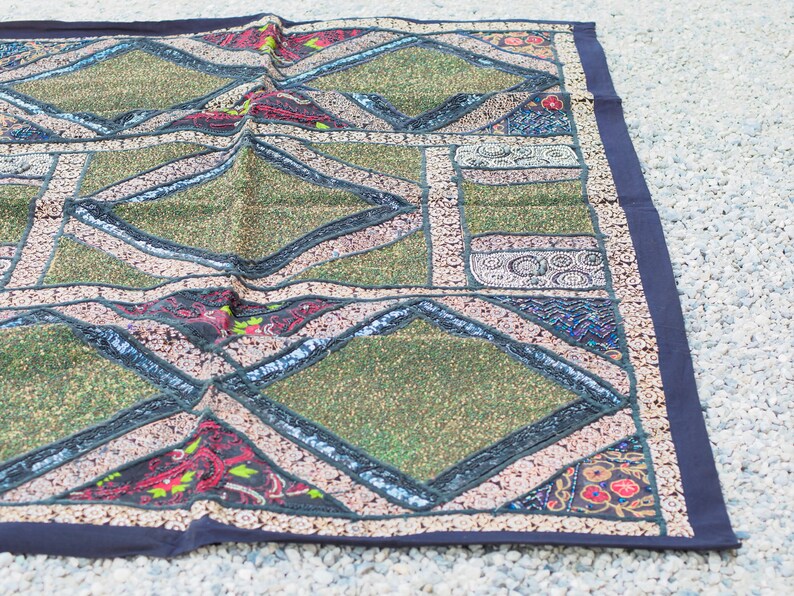 May include: A green and black patchwork throw rug with diamond patterns and intricate embroidery. The rug has a dark blue border.