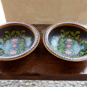 Puede incluir: Dos cuencos de madera negra con un borde blanco y un diseño floral pintado en verde, rosa y azul.