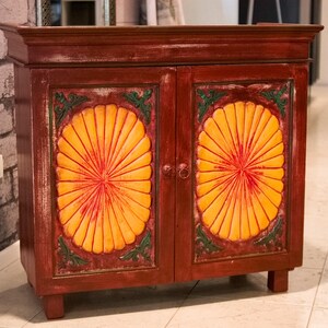 Peut inclure: Un buffet en bois à deux portes avec une finition rouge foncé. Les portes de l'armoire présentent de grands motifs floraux stylisés orange et rouge, encadrés d'accents verts. Le buffet est une pièce de rangement décorative.