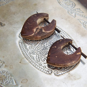 Op de afbeelding: Twee bruine houten hartvormige oorbellen met een zilveren metalen pin.
