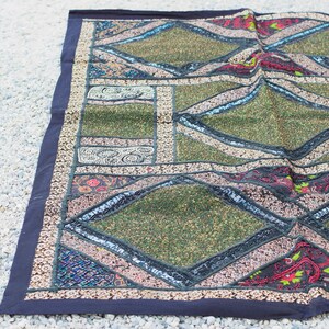 May include: A colorful patchwork rug with a geometric design. The rug is made of different fabrics and textures, including velvet, sequins, and embroidery. The rug is a vibrant mix of green, red, black, and white.