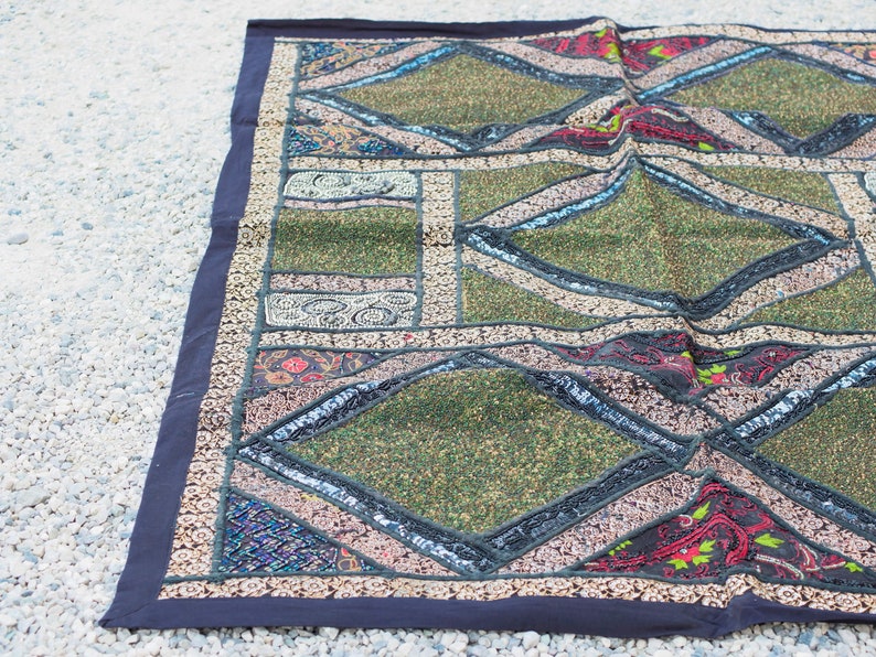 May include: A colorful patchwork rug with a geometric design. The rug is made of different fabrics and textures, including velvet, sequins, and embroidery. The rug is a vibrant mix of green, red, black, and white.