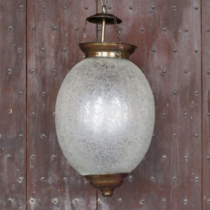 Peut inclure: Un luminaire suspendu en forme de globe en verre givré avec une chaîne en laiton et un sommet en laiton. La lumière est suspendue à un plafond en bois.