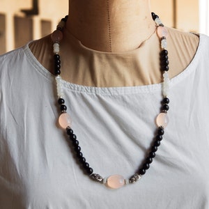 May include: A black and white beaded necklace with pink oval beads. The necklace is made of black onyx, white jade, and rose quartz.