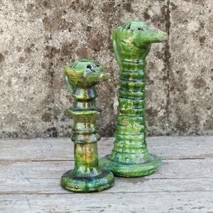 Può includere: Due portacandele in ceramica verde con un design unico. Il portacandele più alto ha una forma cilindrica con un beccuccio in cima. Il portacandele più basso ha una forma di candelabro più tradizionale.