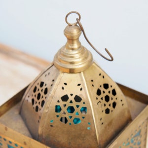 May include: A brass lantern with intricate cut-out designs and a turquoise glass panel. The lantern has a hanging loop and a domed top.