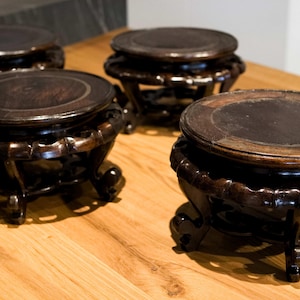 Könnte beinhalten: Vier dunkelbraune Holz-Präsentationsständer mit runden Oberflächen und verzierten Sockeln. Die Ständer stehen auf einer hellen Holzoberfläche, die ihr aufwendiges Design und ihre satte Farbe hervorhebt. Geeignet für dekorative Artikel.