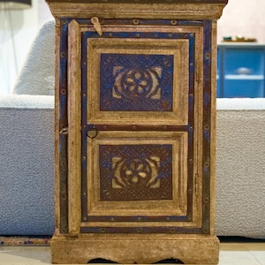 Peut inclure: Petit meuble ancien en bois de forme rectangulaire. Il présente une conception à deux portes avec des motifs floraux bleus et dorés complexes. Le cadre est de couleur marron chaud et le meuble est orné de petits clous métalliques.