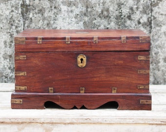 May include: A dark brown wooden box with brass accents and a keyhole. The box has a raised base with a decorative edge.