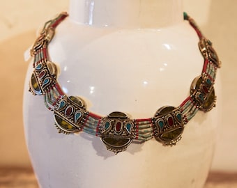 May include: A silver necklace with turquoise, red, and yellow stones. The necklace is made of multiple strands of beads and has a decorative design.