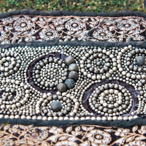 May include: A close-up of a black fabric with silver beads sewn in a circular pattern. The beads are arranged in a swirling design, creating a decorative and intricate look.